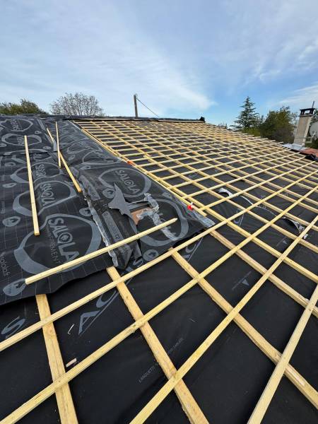 Pose de l'isolation souple sur la toiture par l'extérieur et des liteaux tuile pour le support de la couverture en tuile, par les 2 charpentiers, artisan RGE sur Albi et ses alentours  